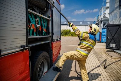 Brandweerman in uniform trekt gereedschap uit brandweerwagen onder een blauwe lucht.