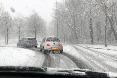 Sneeuw bedekte weg met twee auto’s die voorzichtig draaien in winterse omstandigheden.