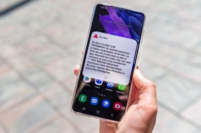 Een hand houdt een smartphone met een NL-Alert testbericht op het scherm.