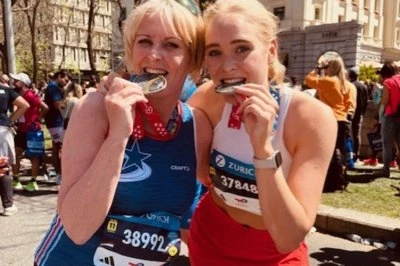 Twee hardlopers met medailles lachen en poseren na de race in een drukke straat.
