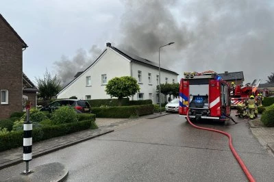 Rook stijgt op achter een woning, brandweerauto met slangen op de weg.