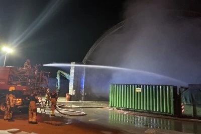 Brandweer blust een vuur bij een grote hal onder een donkere lucht.