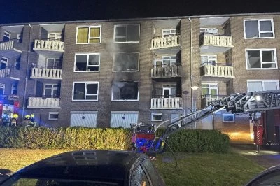 Gebouw met brandvlekken, brandweerauto en brandweerlieden in de nacht.