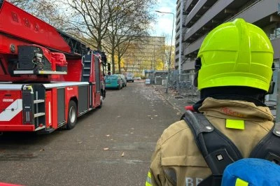 Op deze foto staan een brandweerman en een brandweerauto bij een met lint afgezet appartementenxomplex