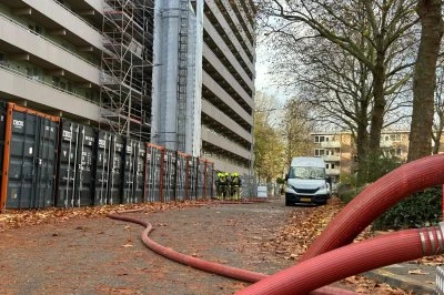 Op deze foto staat een groepje brandweermannen bij het afgezette appartementencomplex, waar ook een brandweerslang naartoe loopt 
